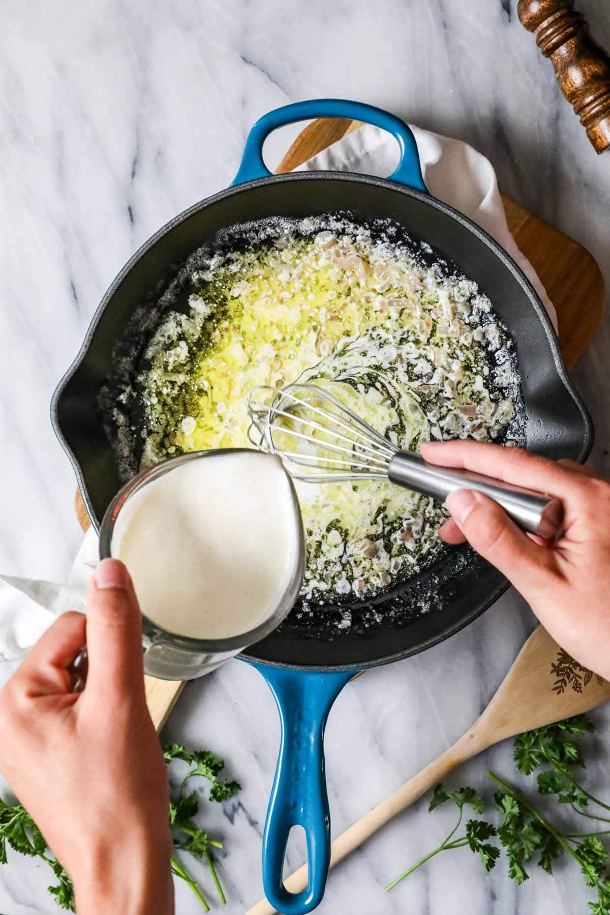 Overhead view of cream being poured into shallots cooking in olive oil and butter.