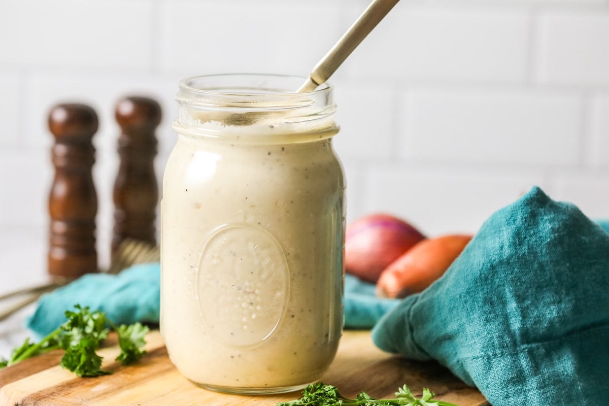 Mason jar filled with a creamy pasta sauce on a wood cutting board.