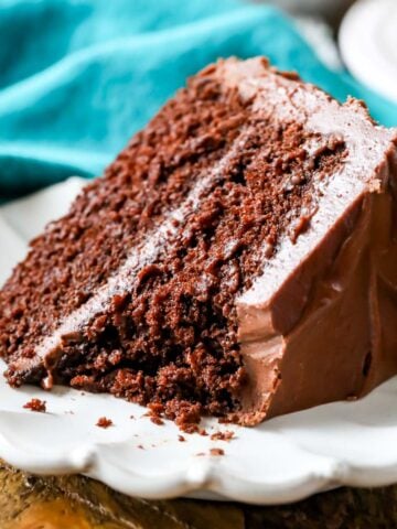 Slice of chocolate cake with one bite missing on a white plate.