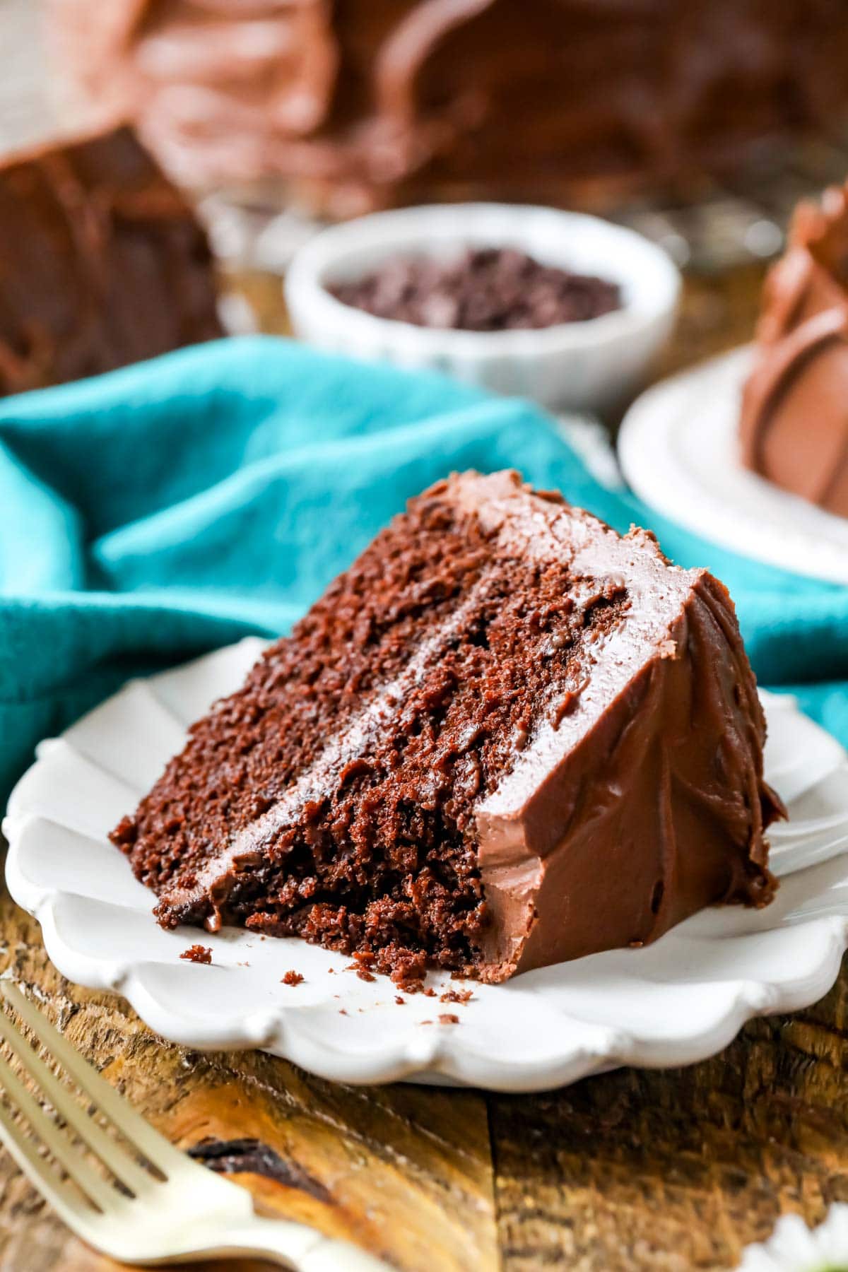 Slice of chocolate cake with one bite missing on a white plate.