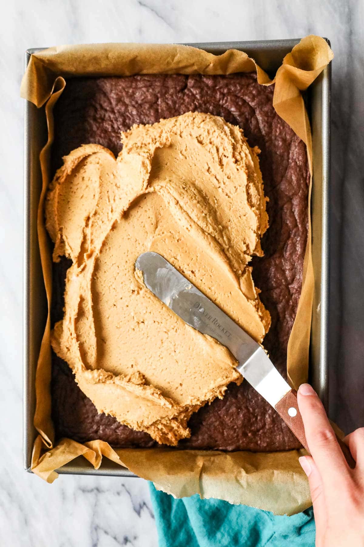 Peanut butter fudge being spread onto a pan of brownies.