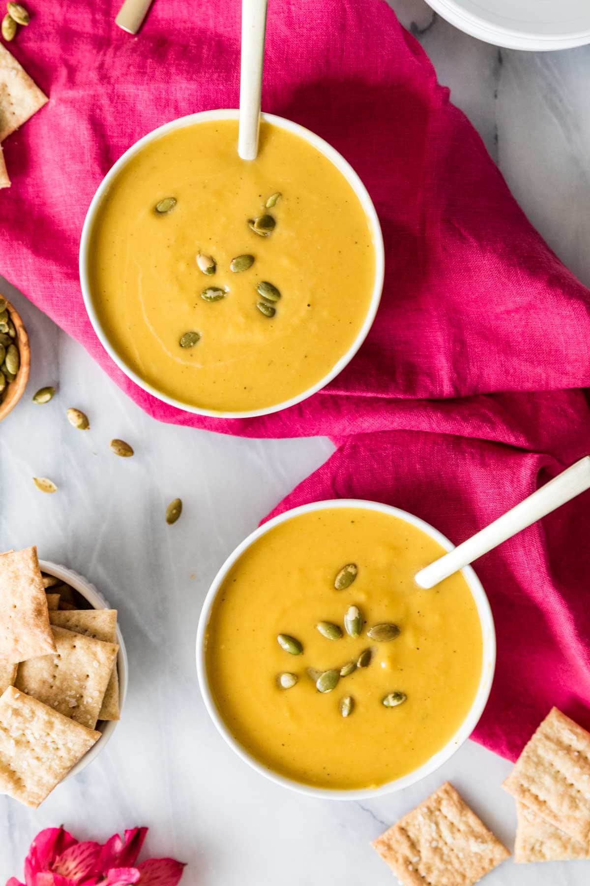 Overhead view of two bowls of a gold colored squash soup topped with pepitas.