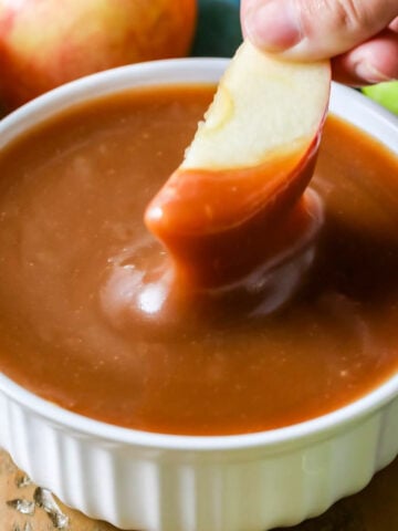 Dipping an apple slice into a white dish full of caramel dip