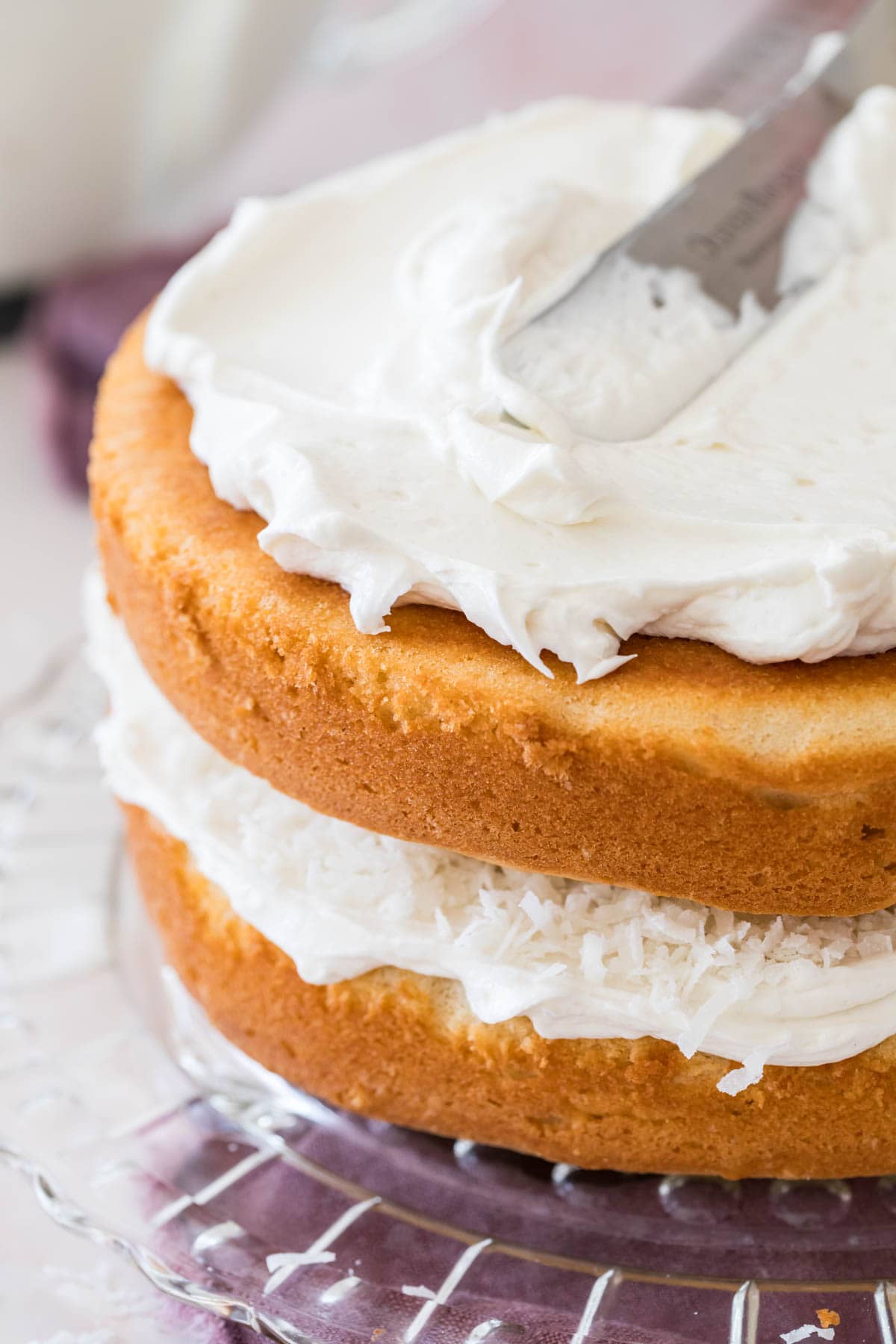 Covering two layers of thick vanilla cake with white frosting