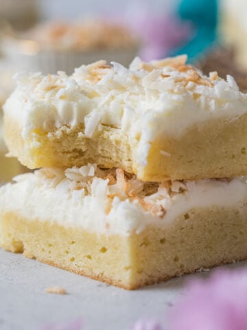 Two coconut cream bars stacked on top of each other, with the top bar missing a bite.
