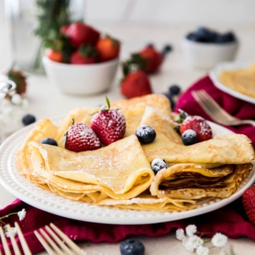 folded crepes with powdered sugar and strawberries on a white plate