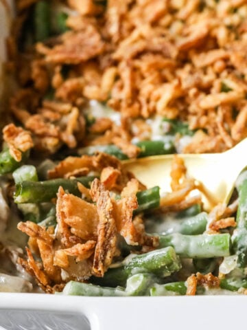 Serving spoon scooping green bean casserole out of a dish.