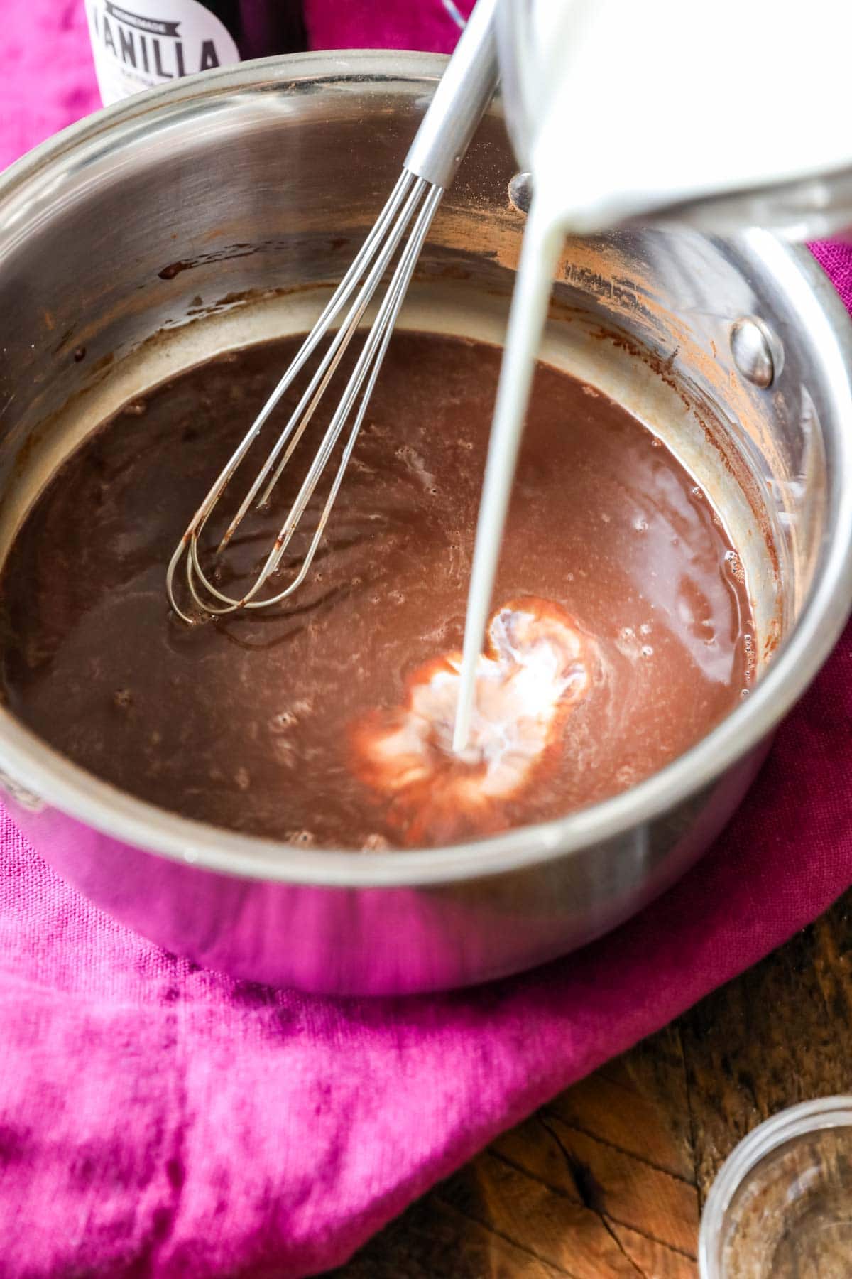 Cream being poured into hot cocoa on the stovetop.