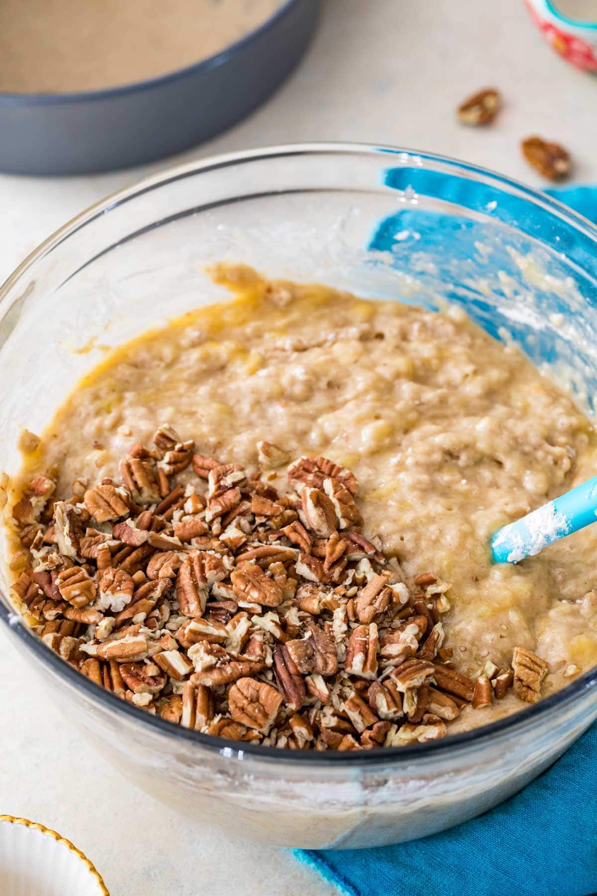 Lumpy cake batter in a glass bowl with pecans added on top, just before stirring