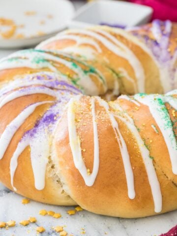 golden brown king cake frosted with white icing and sprinkled with colorful sanding sugars