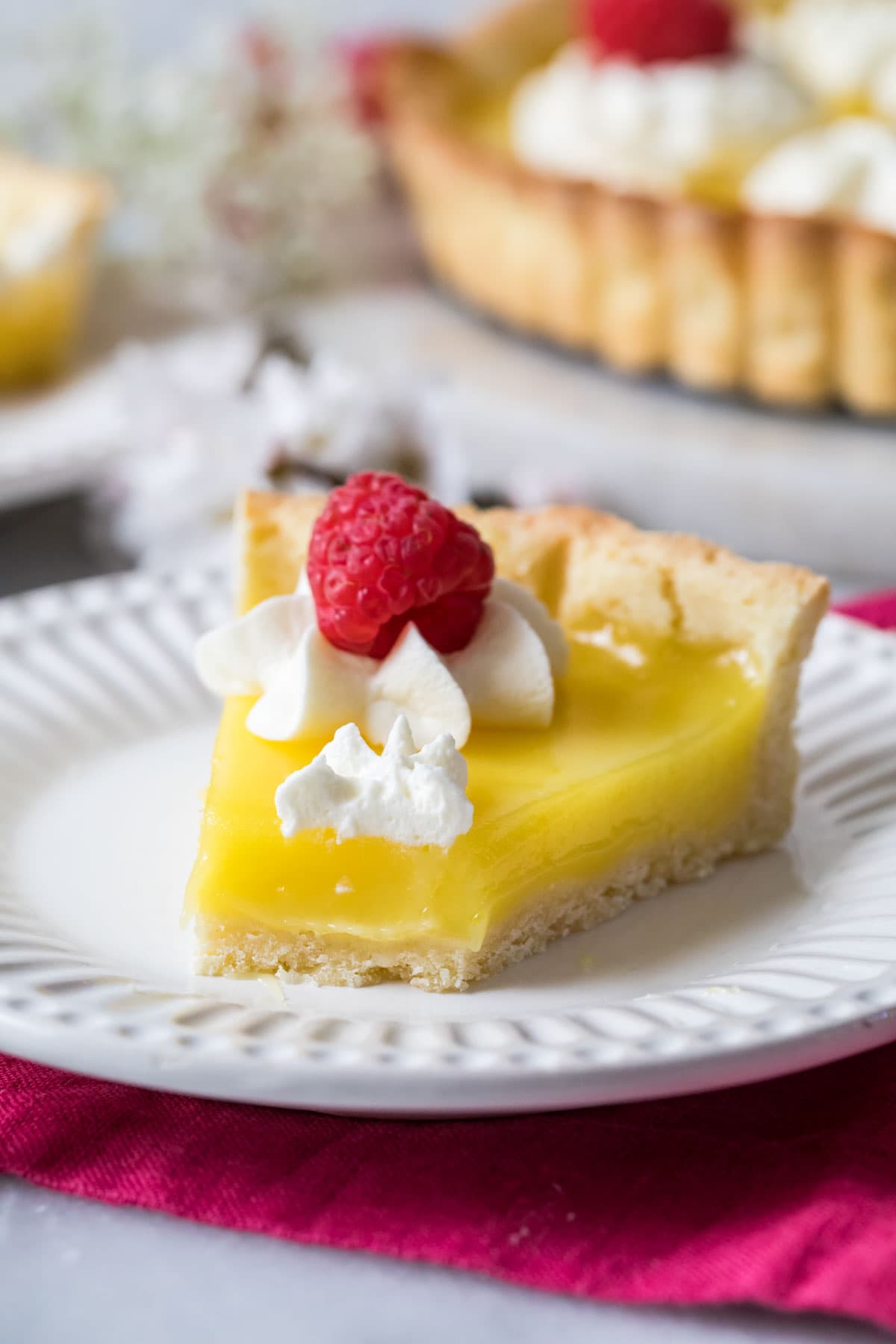 Slice of lemon curd-filled tart missing a bite on a white plate.