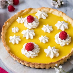 Lemon tart decorated with piped whipped cream and raspberries.