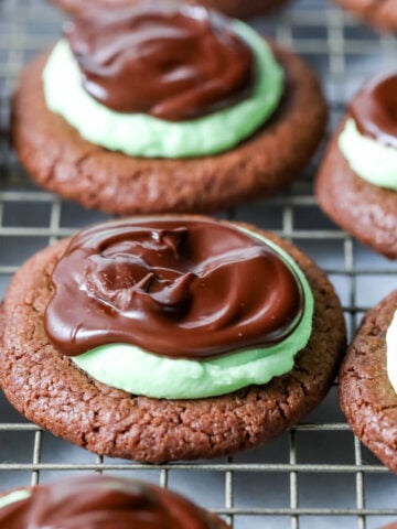 Mint chocolate cookies made with a chocolate cookie base, mint frosting, and chocolate ganache on a cooling rack.