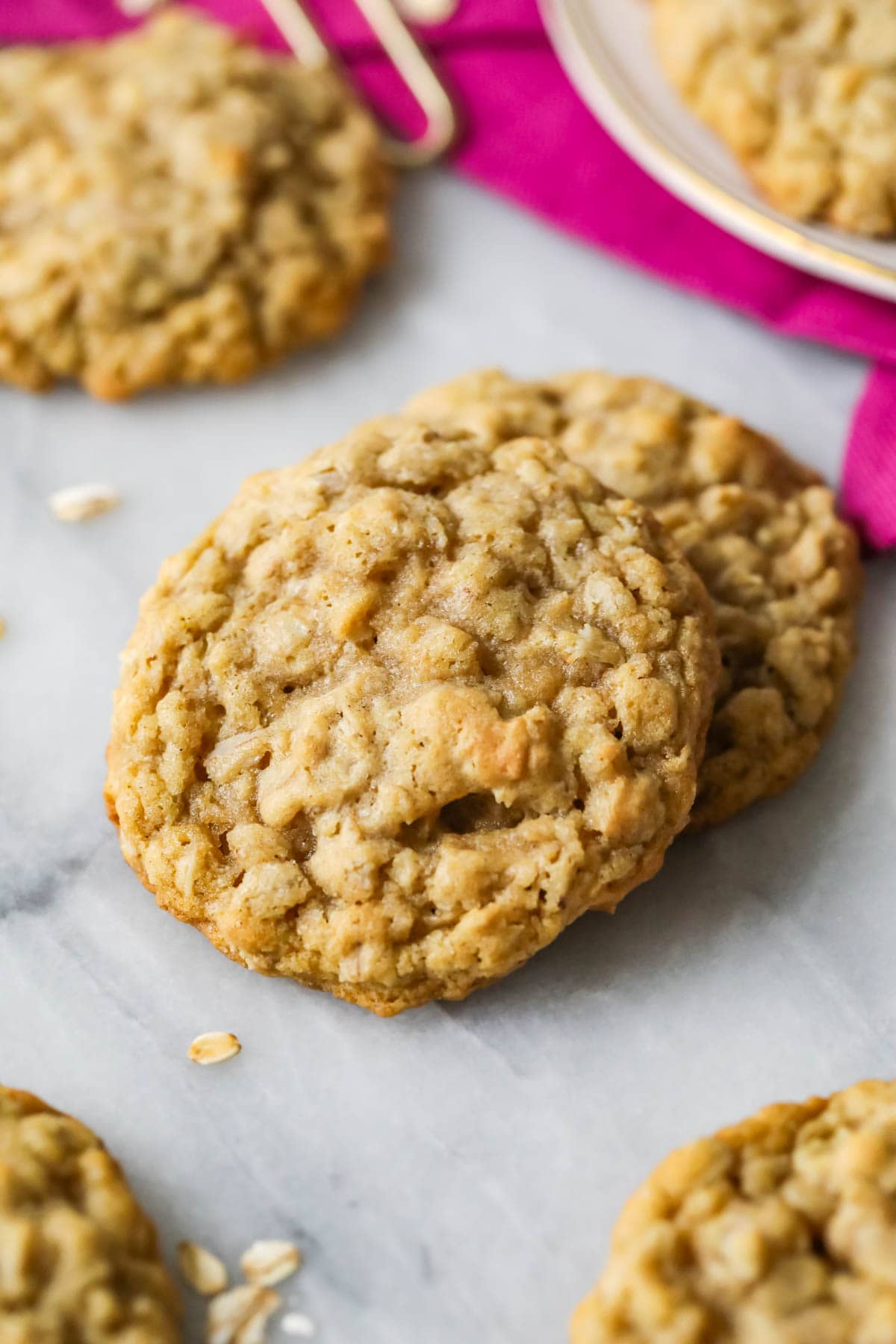 Close-up of two big soft oatmeal cookies on marble, with more cookies in background