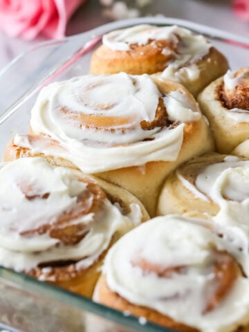 Glass dish of overnight cinnamon rolls frosted with cream cheese frosting.