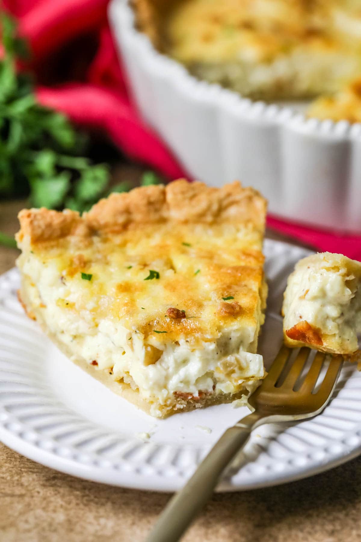Close-up view of a slice of quiche on a plate with one forkful missing.
