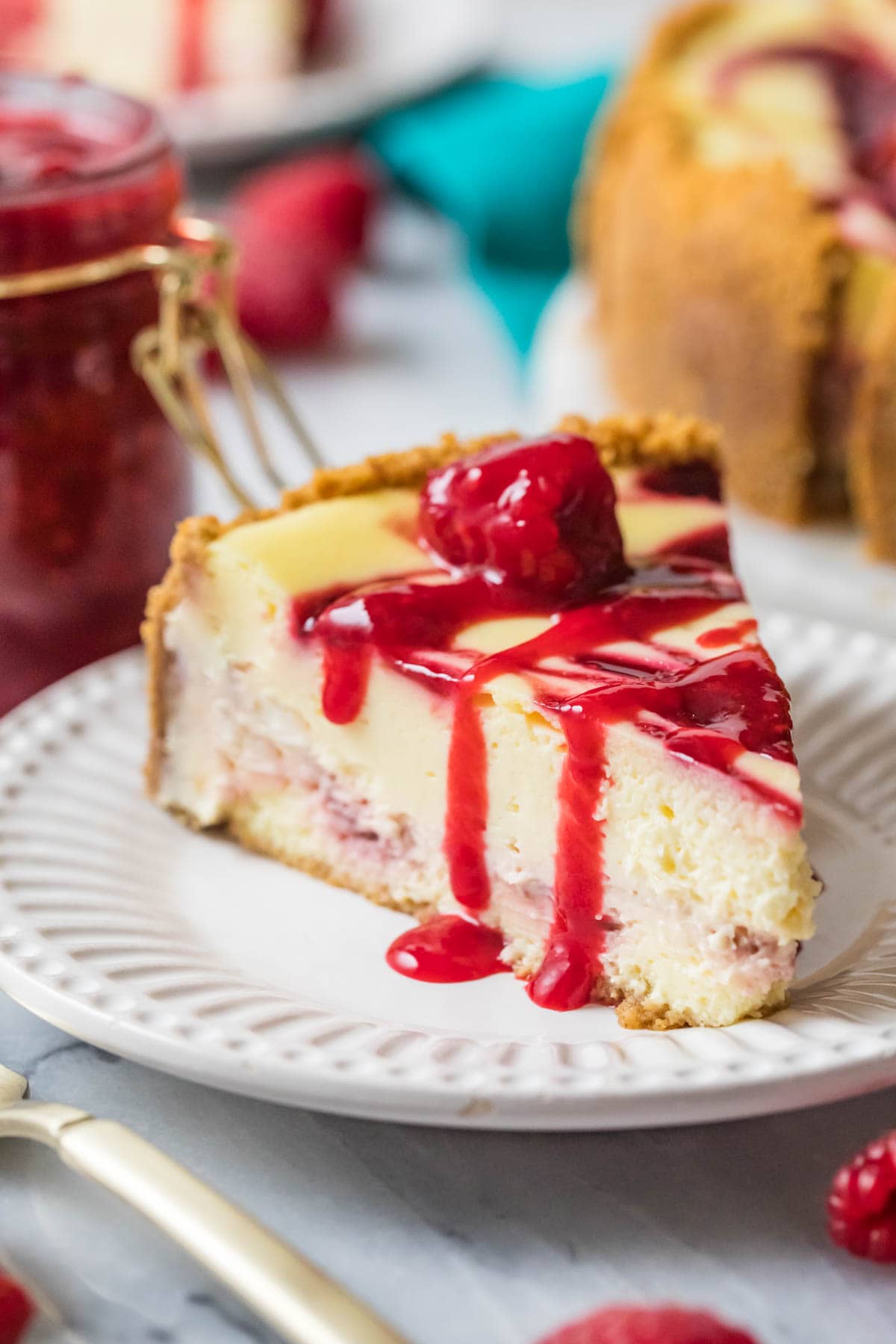 Slice of raspberry cheesecake topped with raspberry sauce on a white plate.