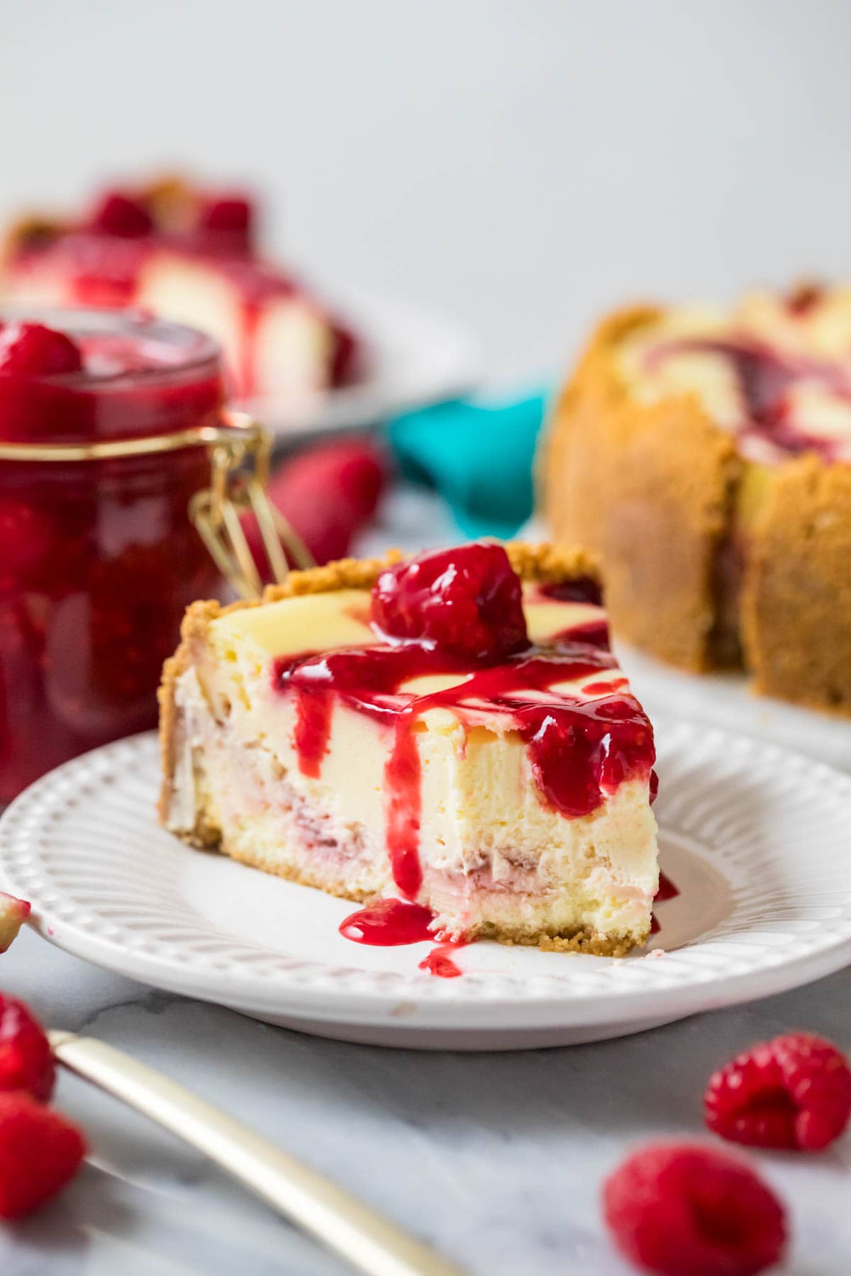 Bite missing from a slice of raspberry cheesecake topped with raspberry sauce on a white plate.