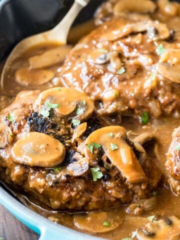 Salisbury steak in a pan with gravy and mushrooms.
