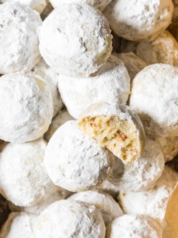Overhead view of snowball cookies in a parchment lined bread pan with one cookie missing a bite.