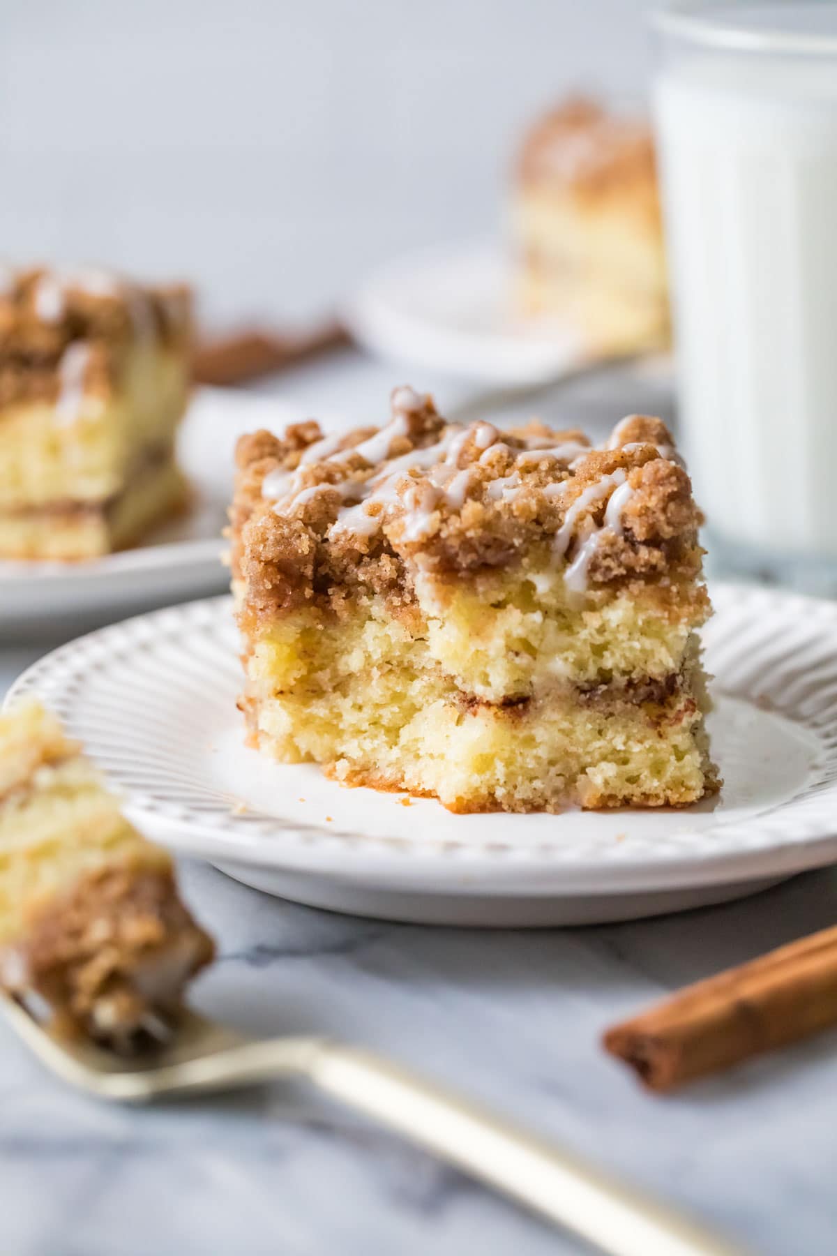 Slice of coffee cake with one bite missing on a white plate.