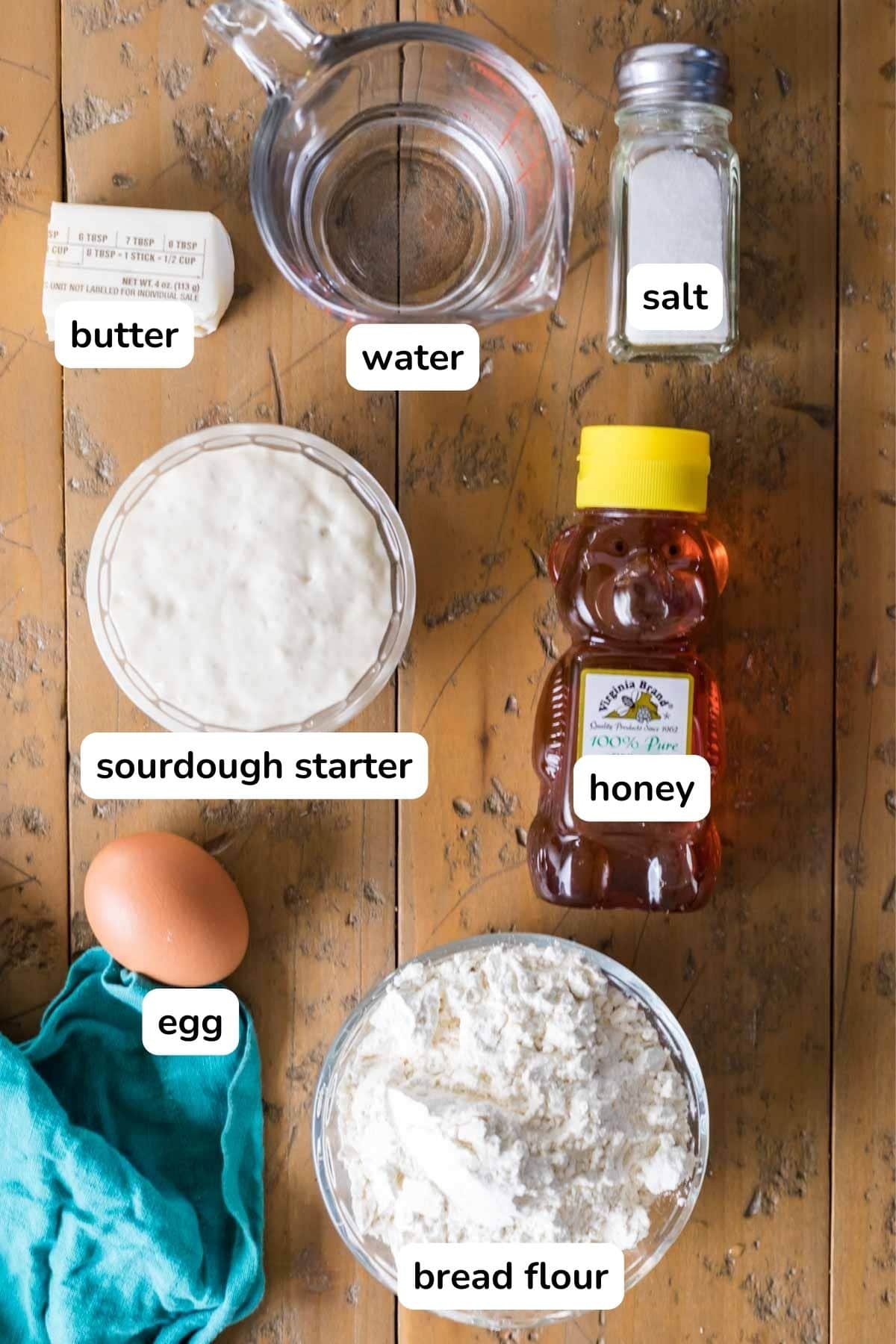 Overhead view of labelled ingredients including sourdough starter, honey, warm water, and more.