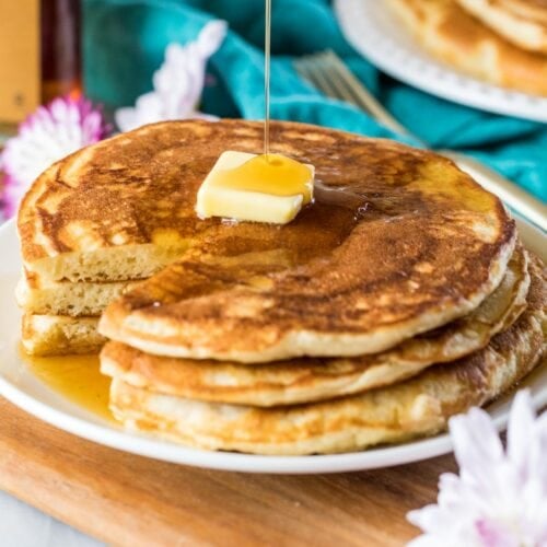Syrup being poured over a buttered stack of sourdough pancakes.