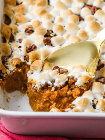 Gold spoon scooping sweet potato casserole out of a white dish.